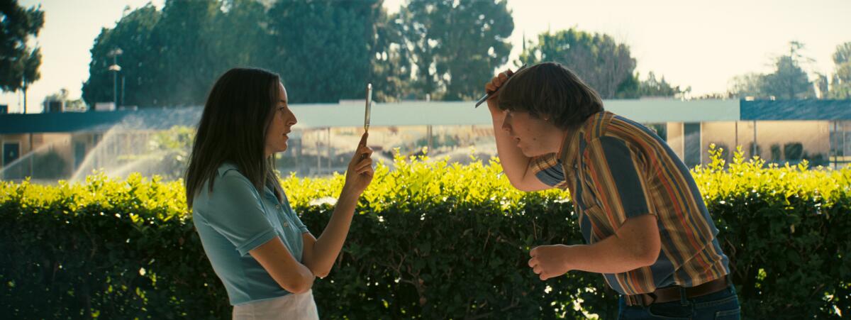 A woman holds a mirror up to a man combing his hair 