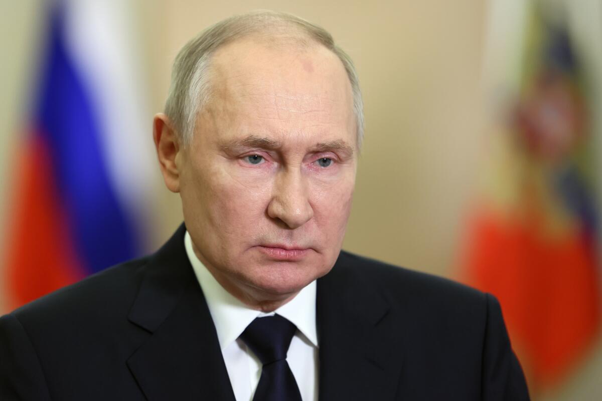 Russian President Vladimir Putin speaks with flags behind him.