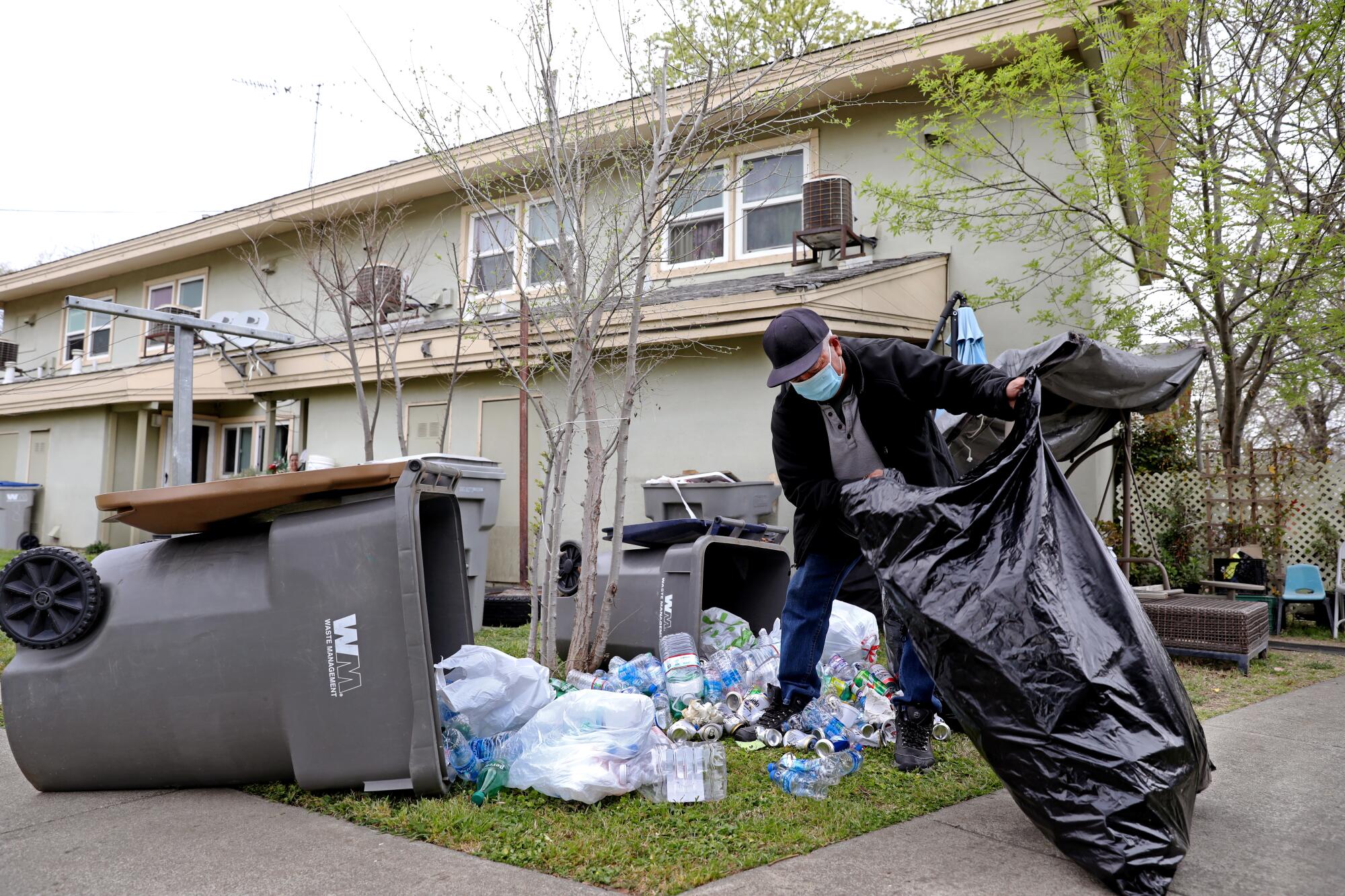 A man gathers recyclables from an overturned trash bin 