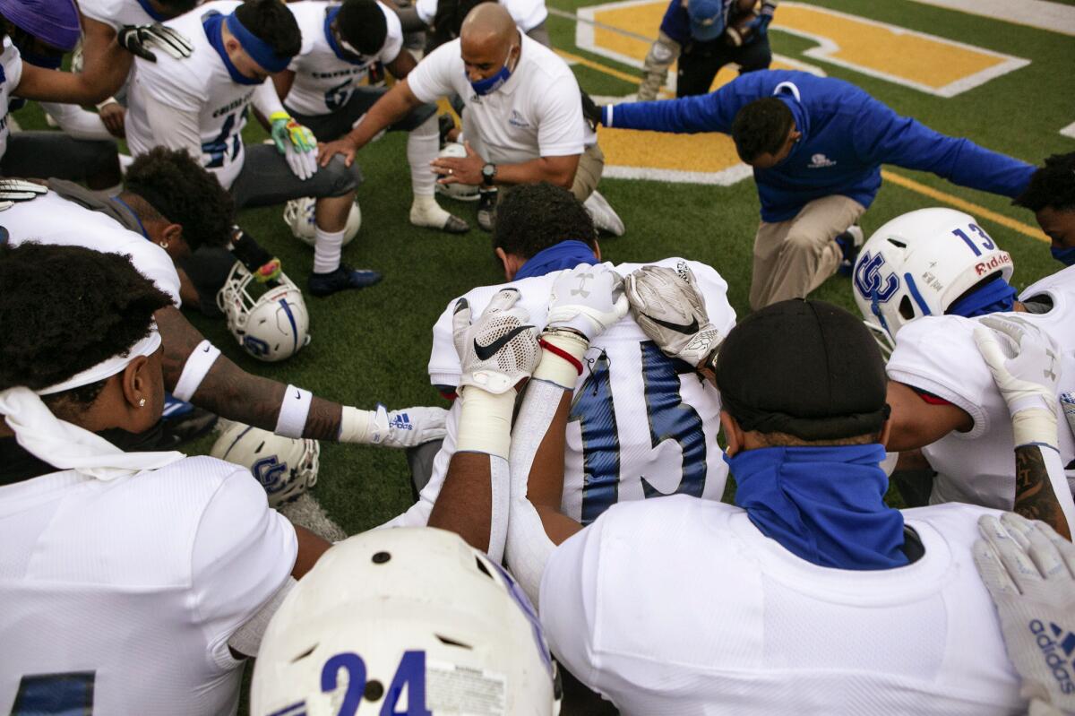 Culver City football coach Jahmal Wright kneels with his team, leading them in prayer 