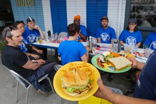 Los Angeles, CA - June 15: A server delivers hot food to a table where a group of striking writers calling themselves "Bike the Strike" are sharing a meal after riding bicycles to Swingers Diner on Thursday, June 15, 2023 in Los Angeles, CA. These photos will accompany a story on the WGA strike and how it affects L.A. restaurants, including the Drew Carey-funded free meals for WGA members at both Swingers Diner and Bob's Big Boy. (Brian van der Brug / Los Angeles Times)