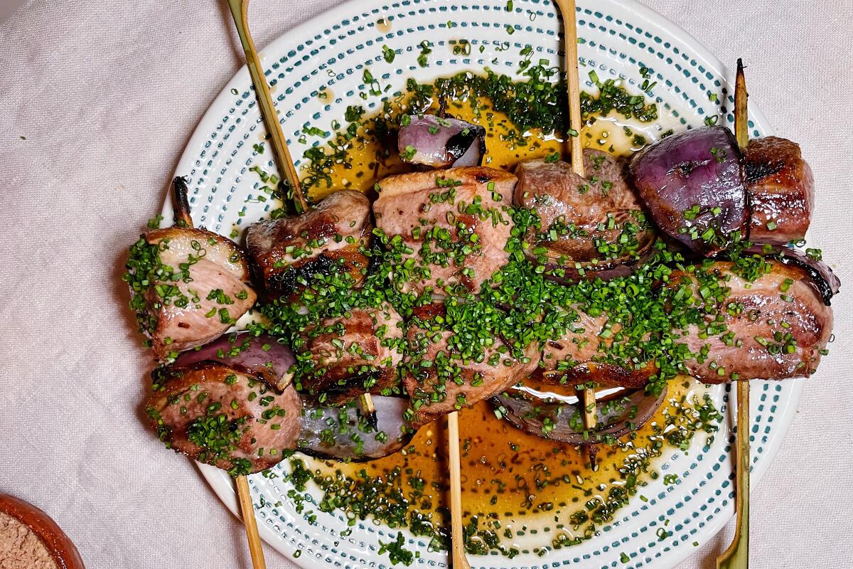 Five duck breast skewers, with black-garlic jus and chives, on a white plate with a dot pattern