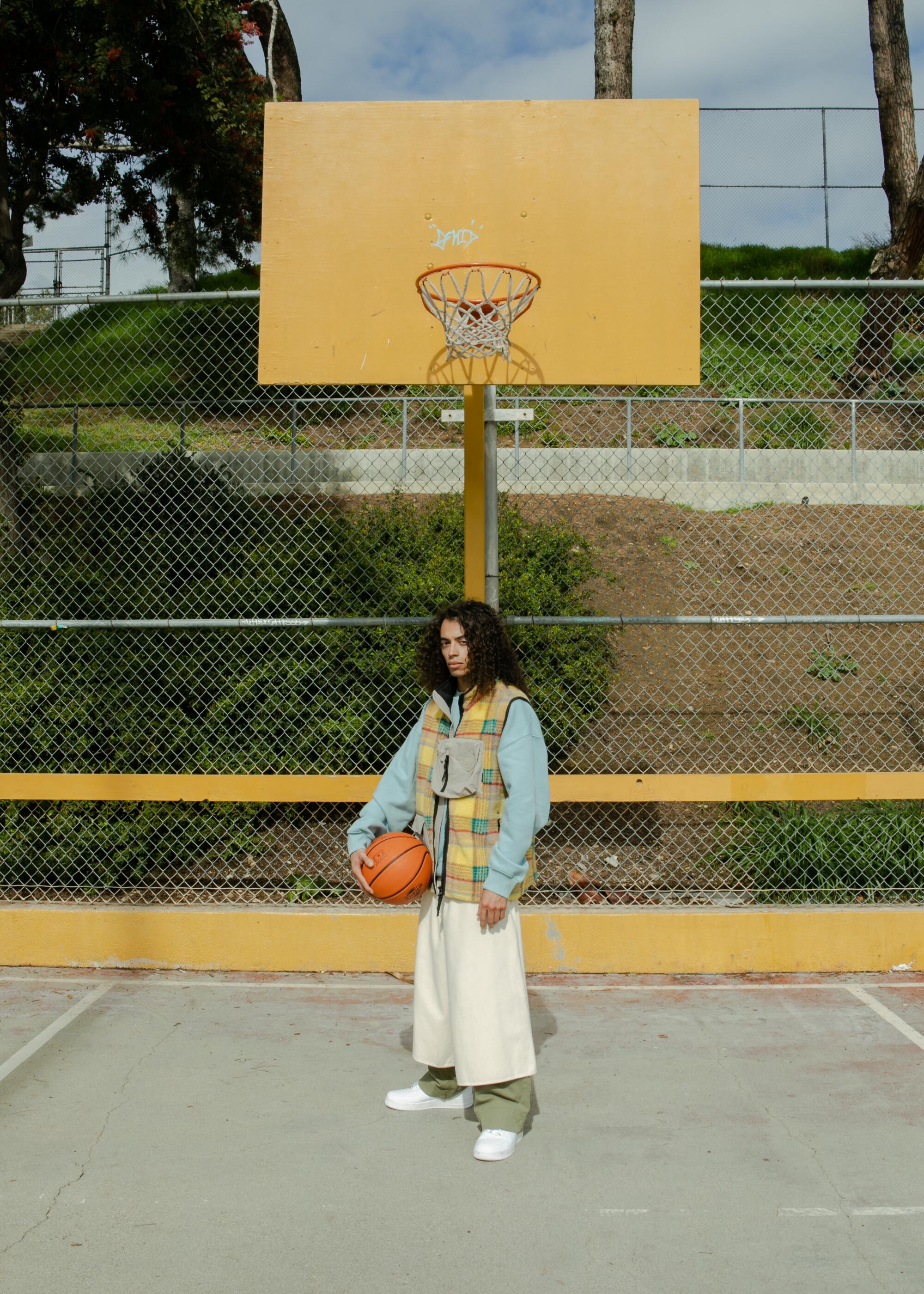 A model holding a basketball wears a plaid vest and loose-fitting outerwear.