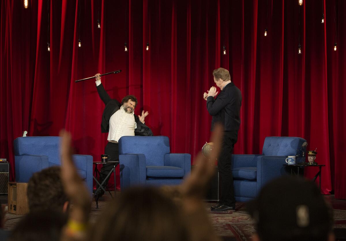 Jack Black raises a cane in the air on the set of "Conan."