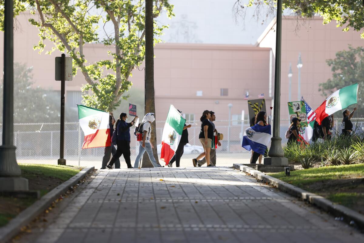 People walk past trees carrying Mexican flags