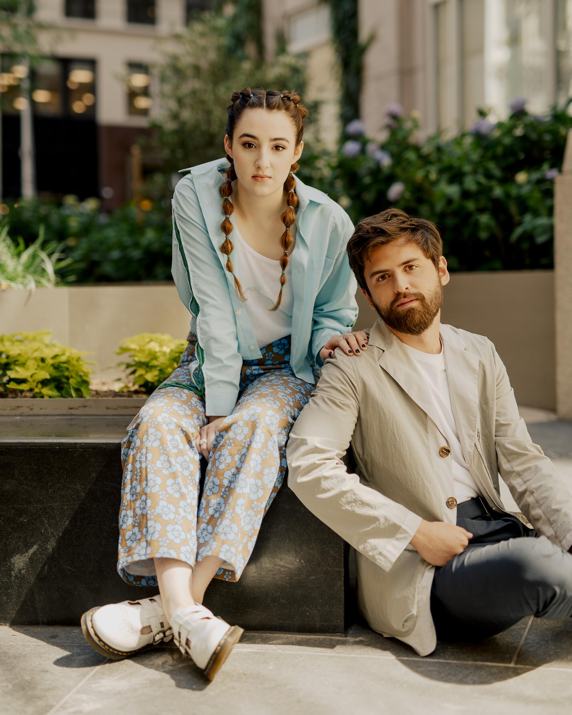 A young woman and man pose seated next to each other.