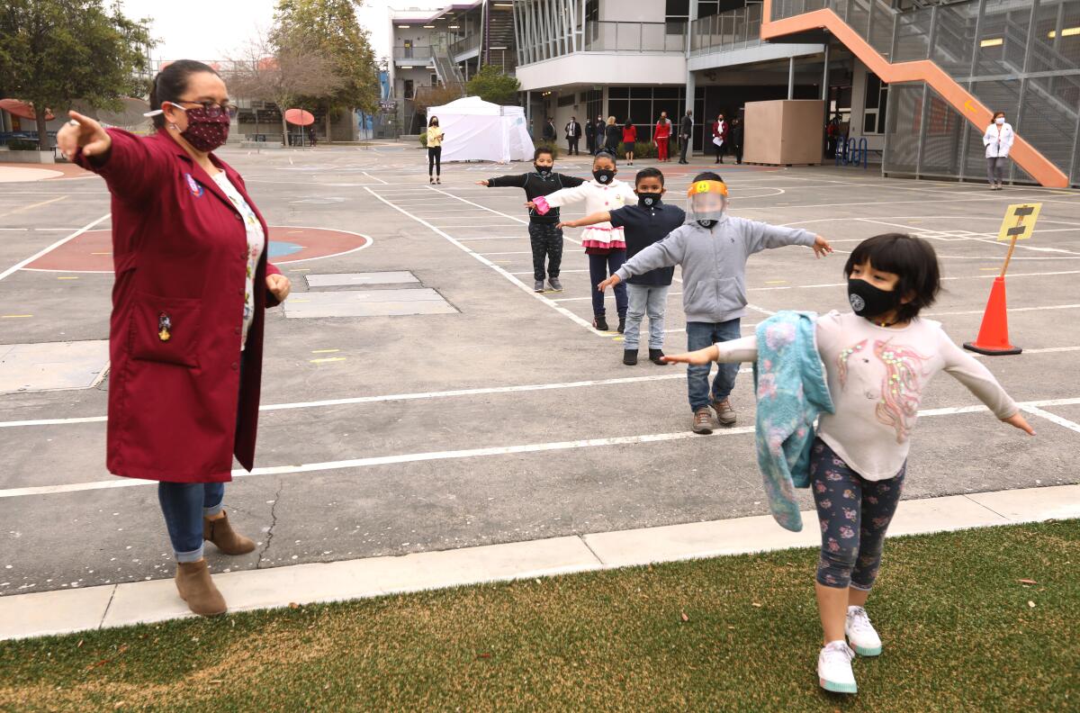 A teacher directing a line of kindergarteners walking at a distance with their arms spread