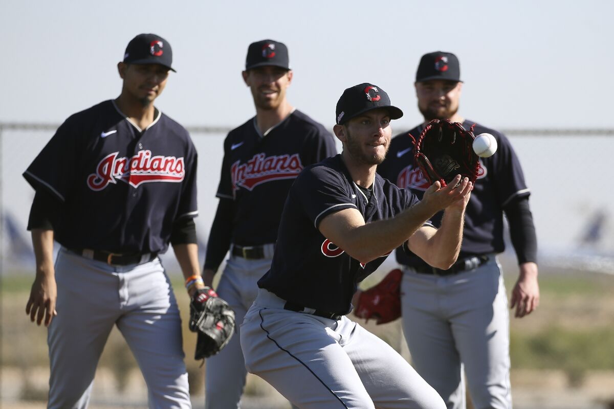 Cleveland Indians pitcher Kyle Dowdy, front, fields a grounder as pitchers Carlos Carrasco, left, Shane Bieber, middle, and Logan Allen, right, look on during spring training baseball workouts for pitchers and catchers Thursday, Feb. 13, 2020, in Avondale, Ariz. (AP Photo/Ross D. Franklin)