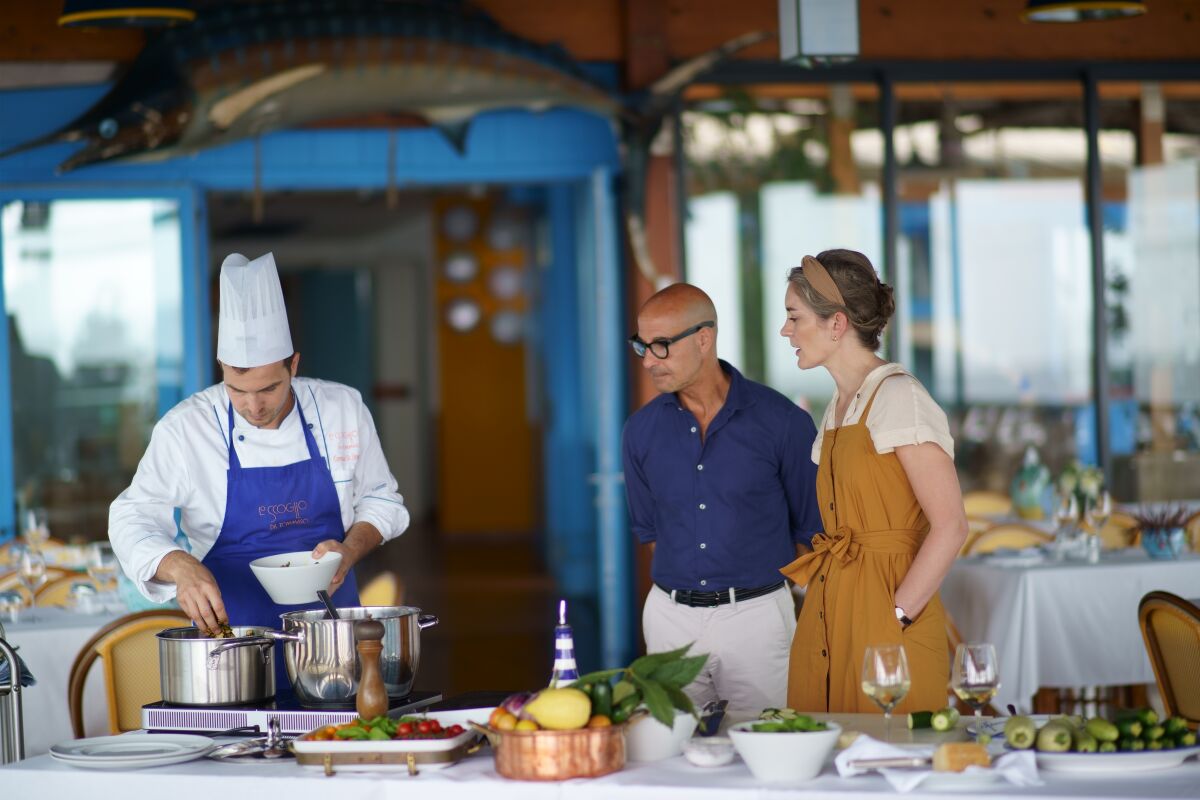 Stanley Tucci and wife Felicity Blunt watch as a chef prepares a meal.