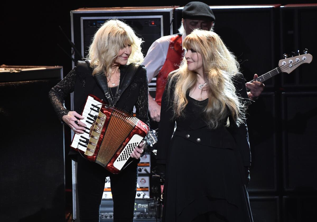 Christine McVie plays an accordion and looks at Stevie Nicks while both are onstage in front of a man playing a guitar