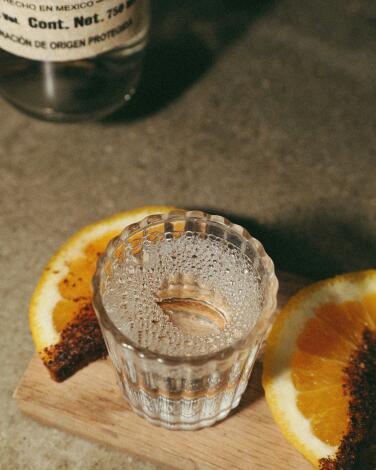 A glass of mezcal with orange slices coated in sal de chapulines from Guelaguetza.