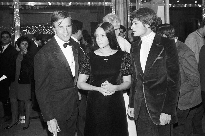 A black-and-white image of a man in a tuxedo standing next to a girl in a velvet dress and a boy in a velvet suit