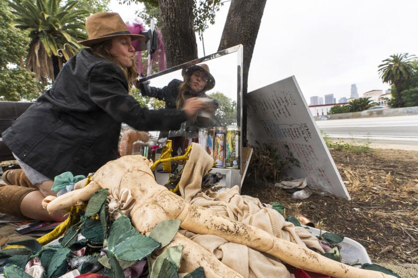 Dawn Woodward, 39, who is homeless and originally from Arizona, dusts a mirror set outdoors in a homeless camp on the side of the CA-101 highway in the Echo Park neighborhood in Los Angeles Tuesday, May 11, 2021. California Gov. Gavin Newsom on Tuesday proposed $12 billion in new funding to get more people experiencing homelessness in the state into housing and to “functionally end family homelessness” within five years. (AP Photo/Damian Dovarganes)
