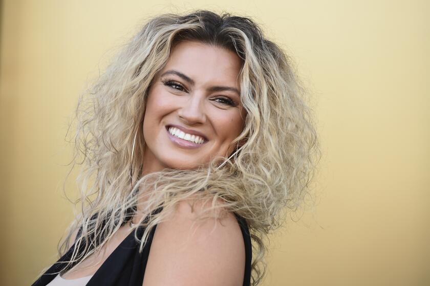 Tori Kelly smiling in a black-and-white outfit against a yellow backdrop.