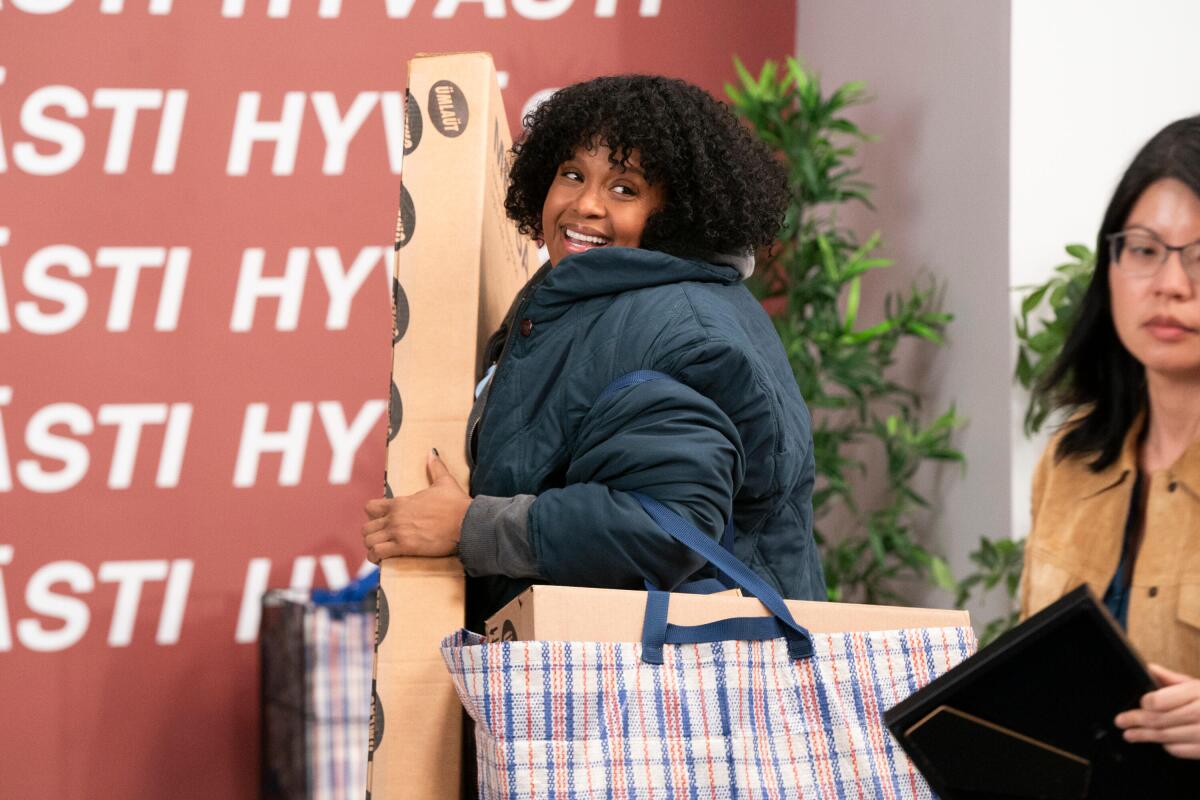 A woman in a blue coat walks out of a store carrying a tall box and two full bags.