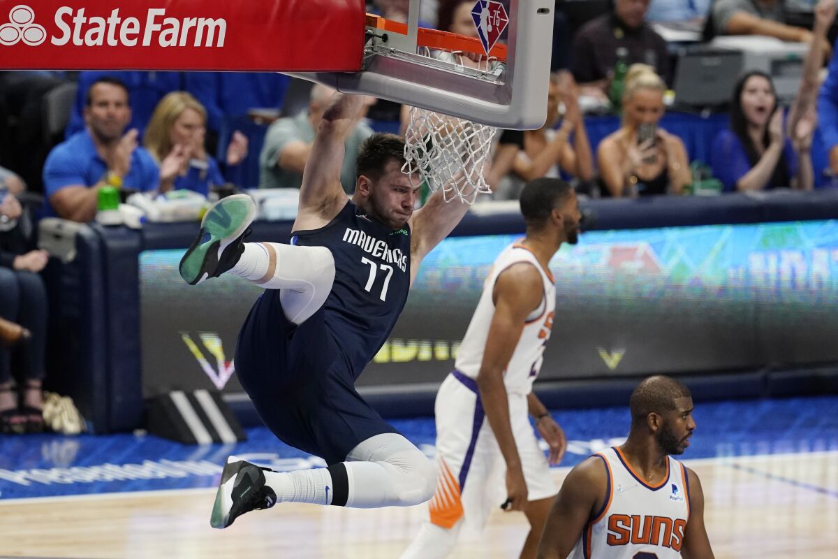 Dallas Mavericks guard Luka Doncic (77) hangs on the rim over Phoenix Suns guard Chris Paul, right, after scoring during the second half of Game 6 of an NBA basketball second-round playoff series, Thursday, May 12, 2022, in Dallas. (AP Photo/Tony Gutierrez)