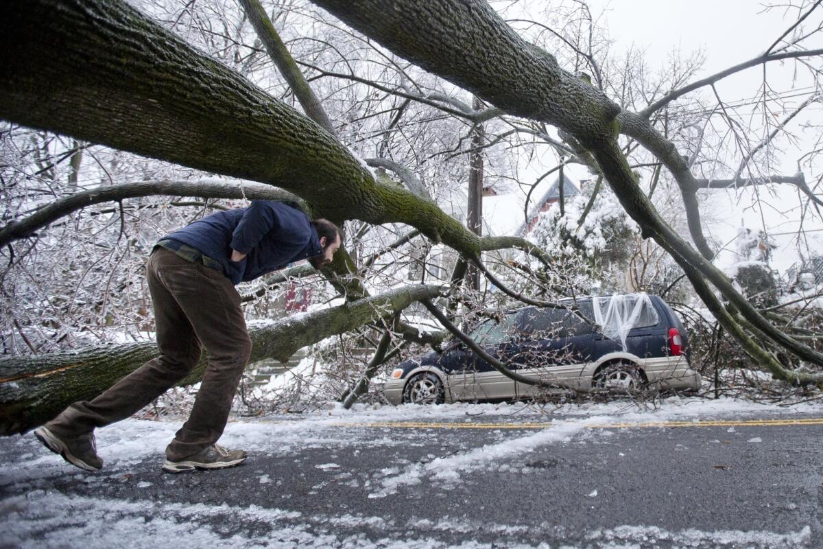 A man inspects an ice-covered downed tree that took out a utility line and landed atop a minivan in Philadelphia, after the city was slammed by a winter storm. Utility crews aren't getting much relief from the weather as they work to restore electricity to hundreds of thousands of people in Pennsylvania and Maryland.
