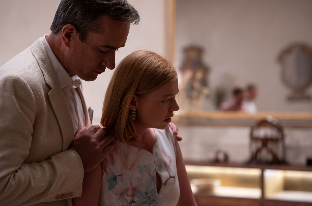 A man rests his hands on woman's shoulders as she looks away in distress