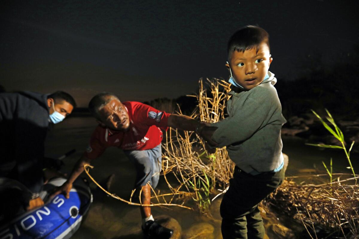 A boy looks over his shoulder as he stands alongside the shore of a river.