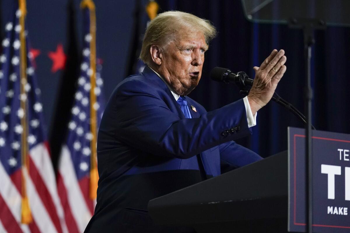 Former President Trump gesturing while speaking from a lectern in front of a row of American flags