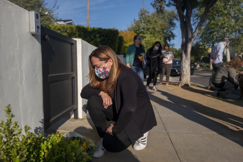A woman kneels in front of flowers placed outside a home's front gate