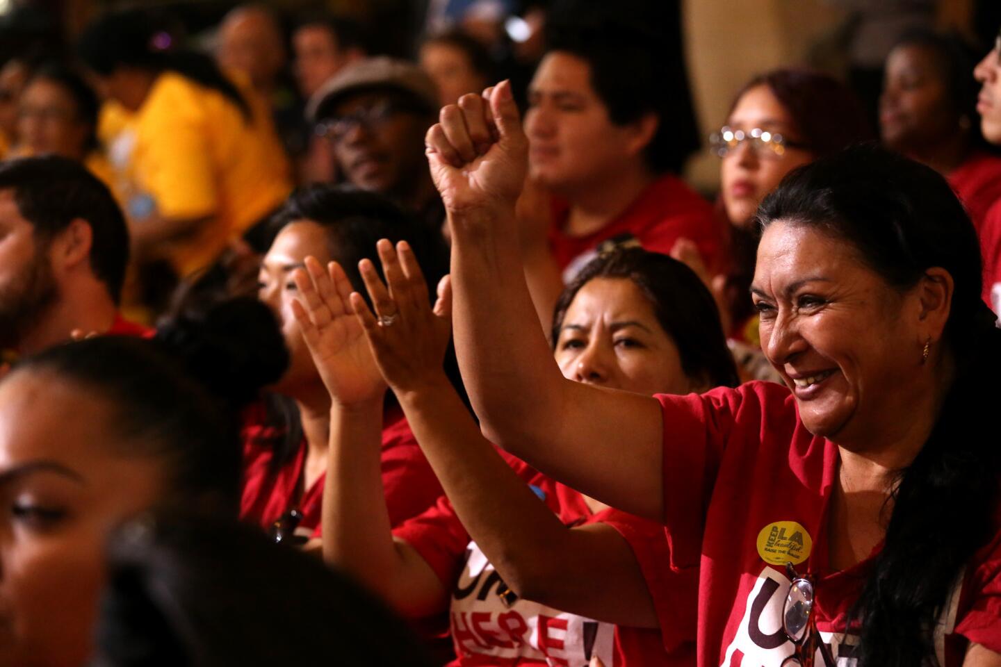 Maria Castaneda, with Unite Here, raises her fist as others applaud a speech of support for raising the minimum wage.