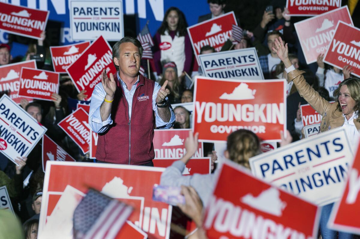 Republican gubernatorial candidate Glenn Youngkin walks onstage to address supporters carrying signs.
