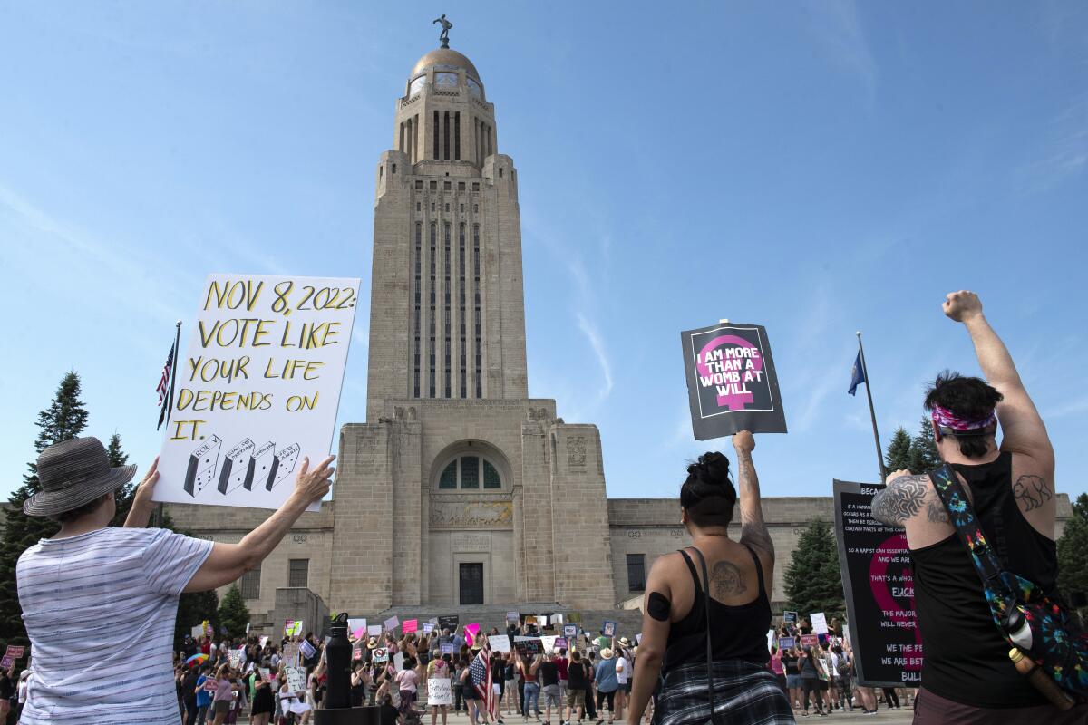 Protesters hold signs in front of the Nebraska State Capitol.