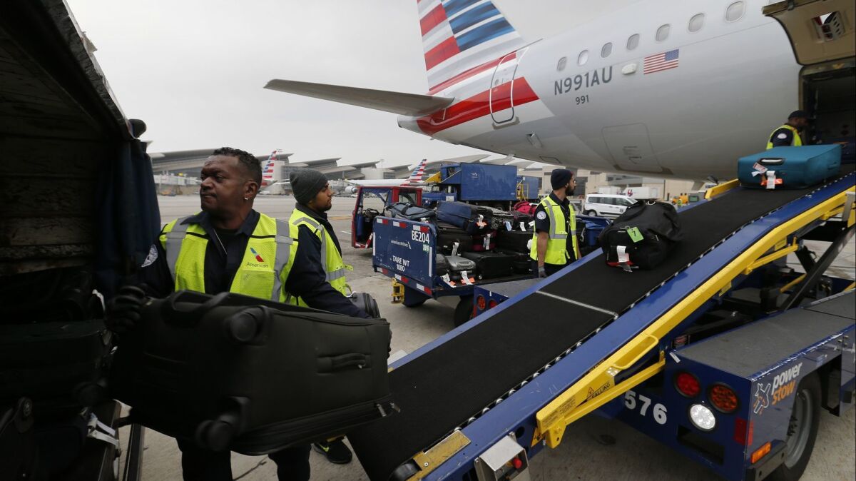 Workers unload bags from an American Airlines flight at Los Angeles International Airport. The average domestic airfare dropped to its lowest inflation-adjusted level since at least 1995.