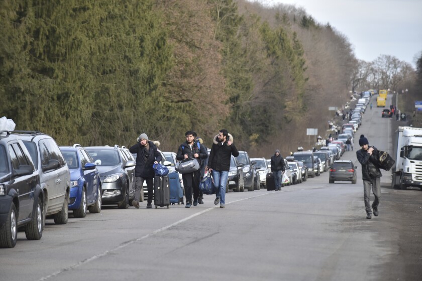 People walk past a queue of cars heading to the Poland border near Shehyni, western Ukraine, Tuesday, March 1, 2022. Russian shelling pounded civilian targets in Ukraine's second-largest city again, and a 40-mile convoy of tanks and other vehicles threatened the capital. Ukraine's embattled president said the tactics were designed to force him into concessions in Europe's largest ground war in generations. (AP Photo/Pavlo Palamarchuk)