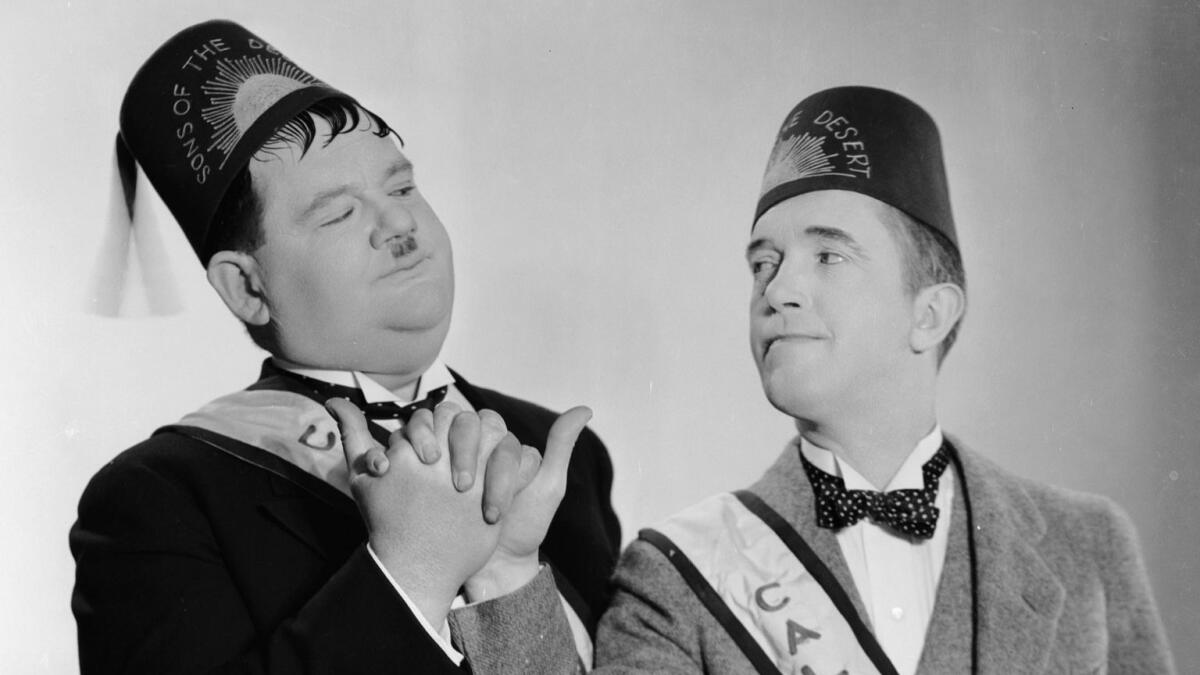 In ceremonial fez and sash, Stan Laurel and Oliver Hardy engage in a Masonic-style handshake dressed as they appear in the 1933 movie 'Sons Of The Desert,' directed by Lloyd French and William A Seiter.
