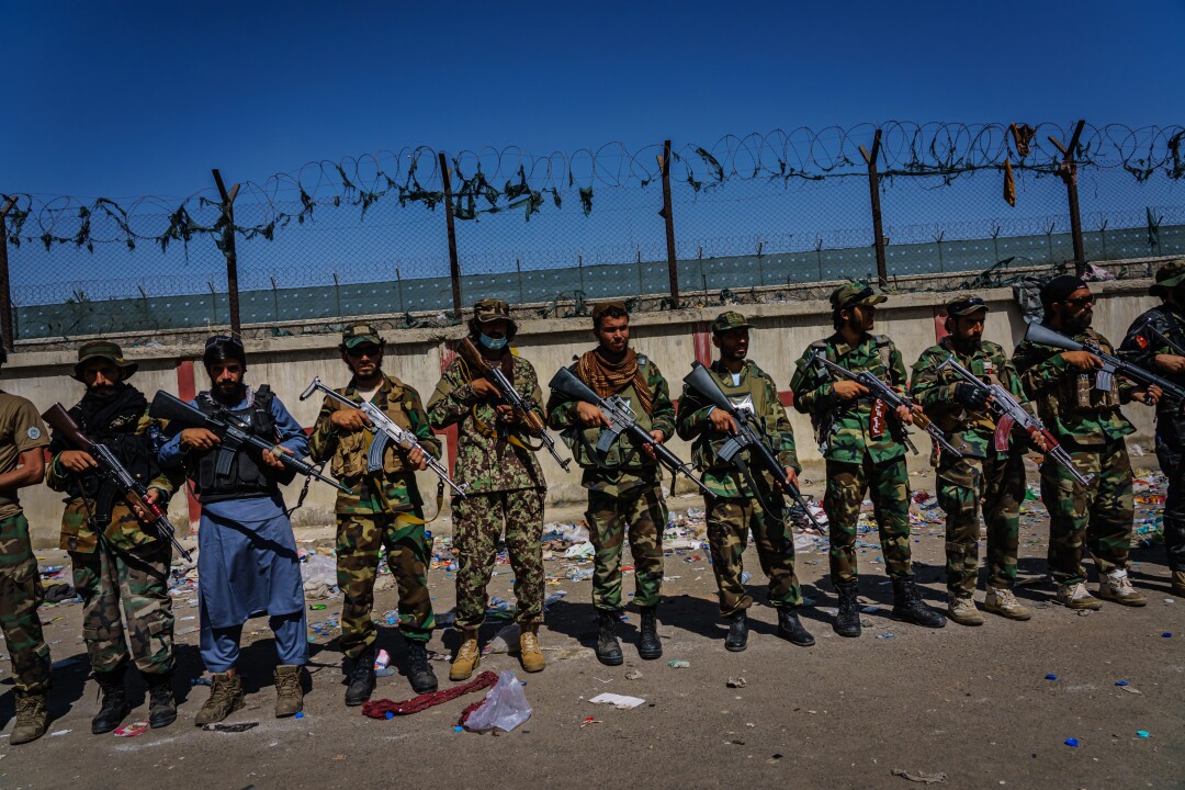 رزمندگان طالبان با اسلحه در مقابل حصار صف آرایی می کنند