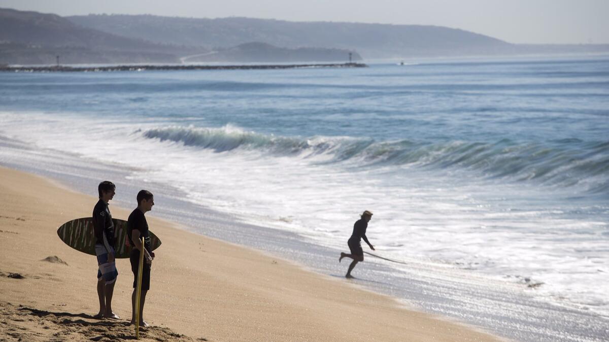 Skimboarders look for waves Tuesday on an unusually hot day in Newport Beach. Temperatures reached more than 100 degrees in the city, breaking the record of 85 degrees for the date, set in 1965.