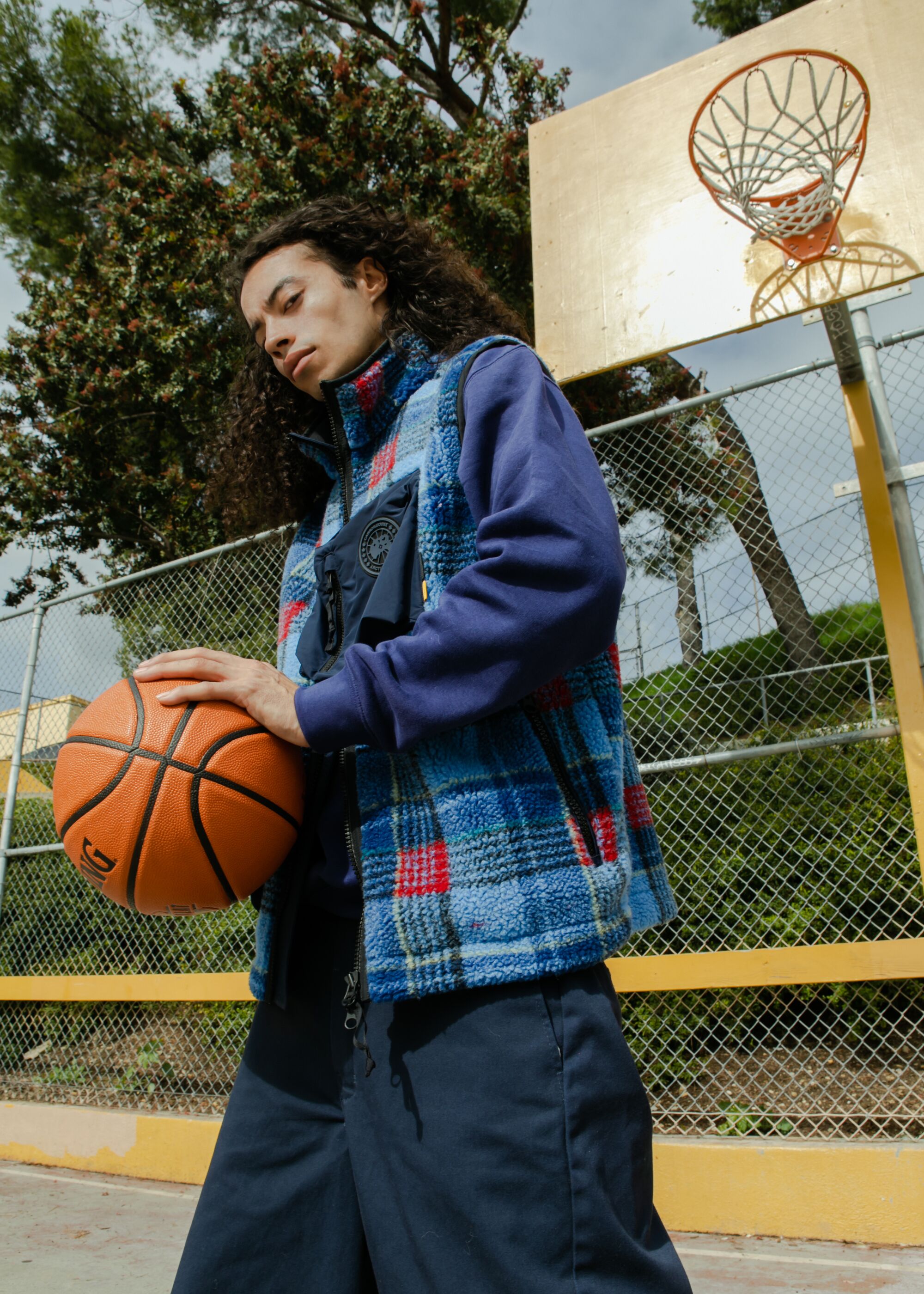 A model wearing a blue tartan vest palms a basketball.