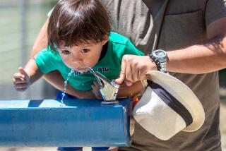 CANOGA PARK, CA-JULY 10, 2023: Abe Perez lifts his 2 year old son Mavy, so he can successfully get a drink of water from a fountain at Lanark Park in Canoga Park on a hot, Monday afternoon. (Mel Melcon / Los Angeles Times)