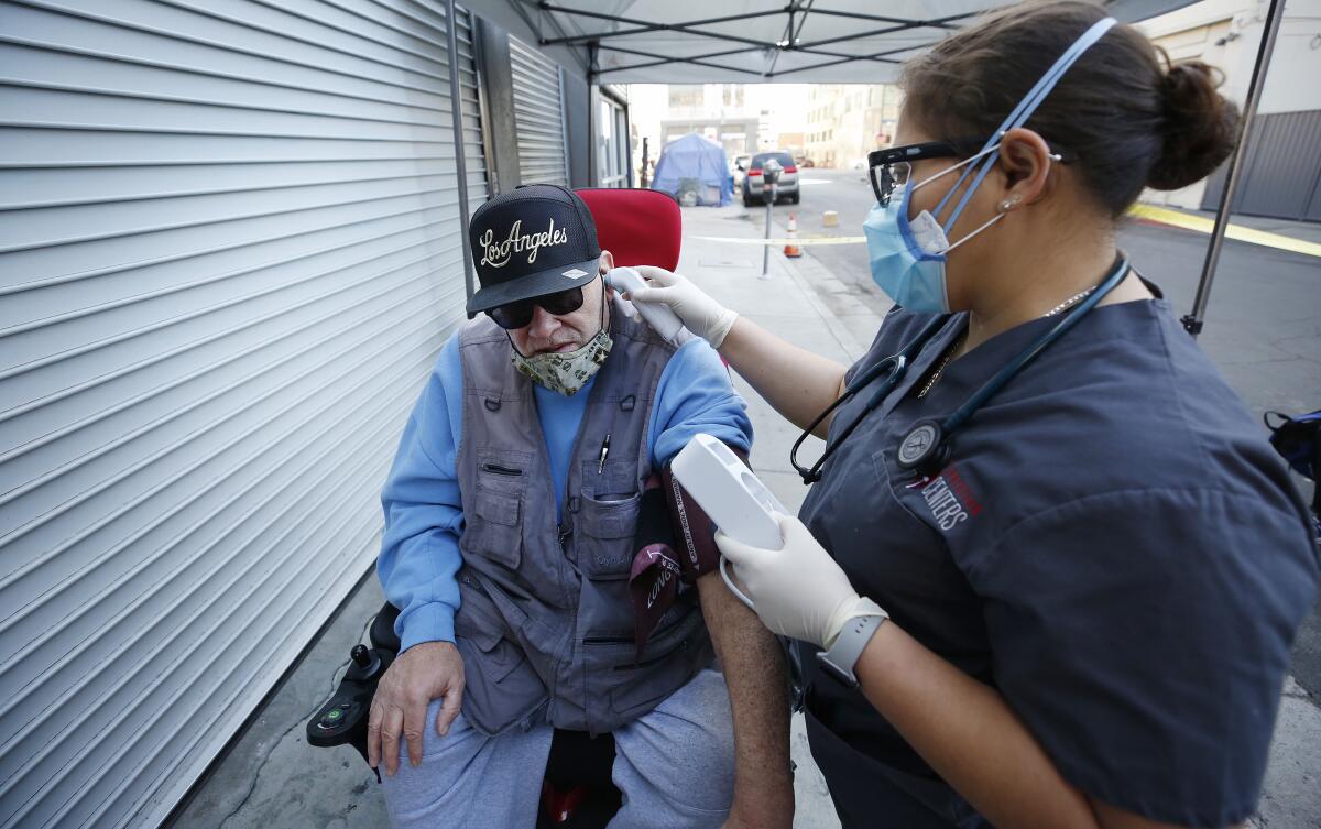 A healthcare worker places a thermometer in the ear of a man in a wheelchair