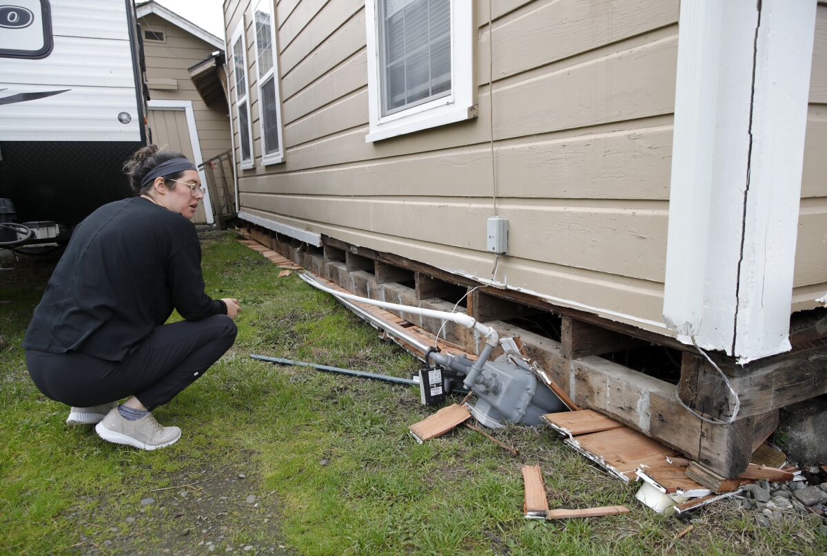 Seorang wanita memeriksa fondasi rumah yang rusak.