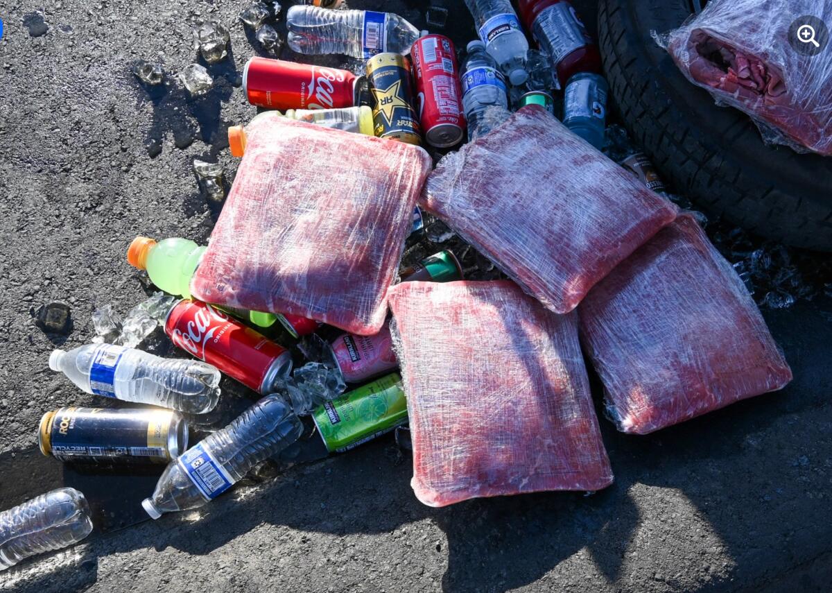 Beverage bottles and cans and plastic-wrapped meat lie on a highway shoulder.