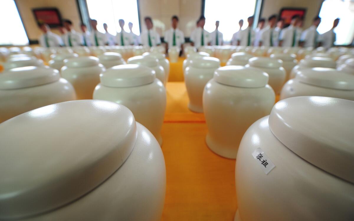 Attendants stand behind a display of biodegradable urns at a cemetery in Tianjin, northern China on July 20, 2010.