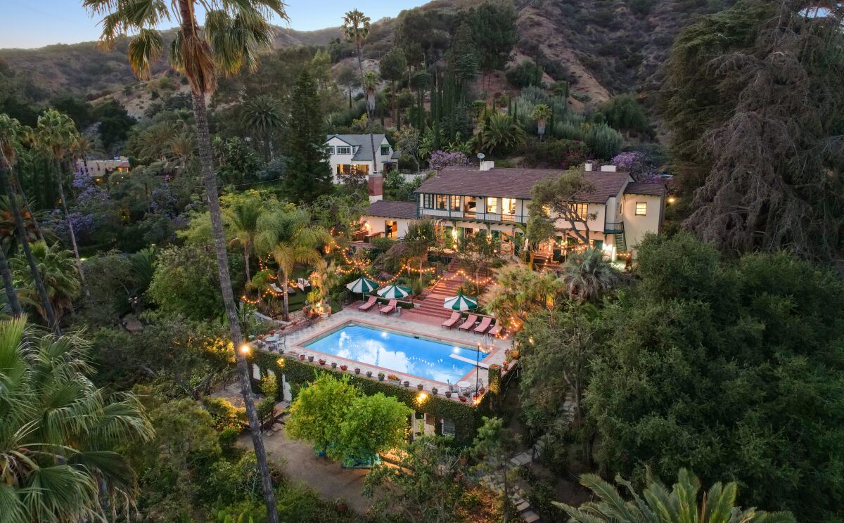 A home with manicured gardens lined by string lights and with an outdoor pool.