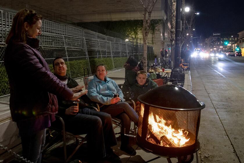 PASADENA, CA - DECEMBER 31, 2019: Denise Koehnlein of Phoenix, left, stays warms by the fire while chatting with Mark Breiling, Quisha Ryan and Christian Ryan,13, as they camp along the Rose Parade route on Colorado Boulevard on December 31, 2019 in Pasadena, California. .(Gina Ferazzi/Los AngelesTimes)