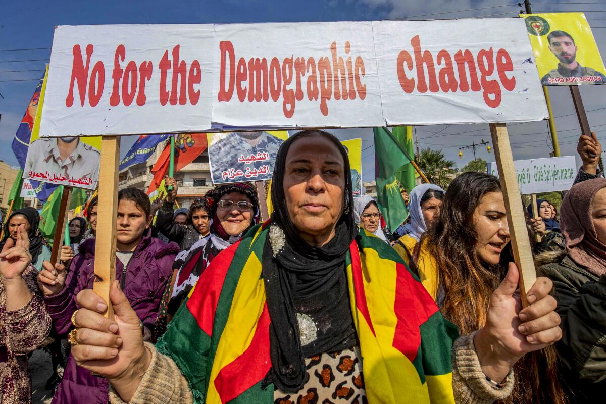 A Syrian Kurdish woman holds a sign during a protest in Qamishli, Syria, against Turkey's military advance into Syria.