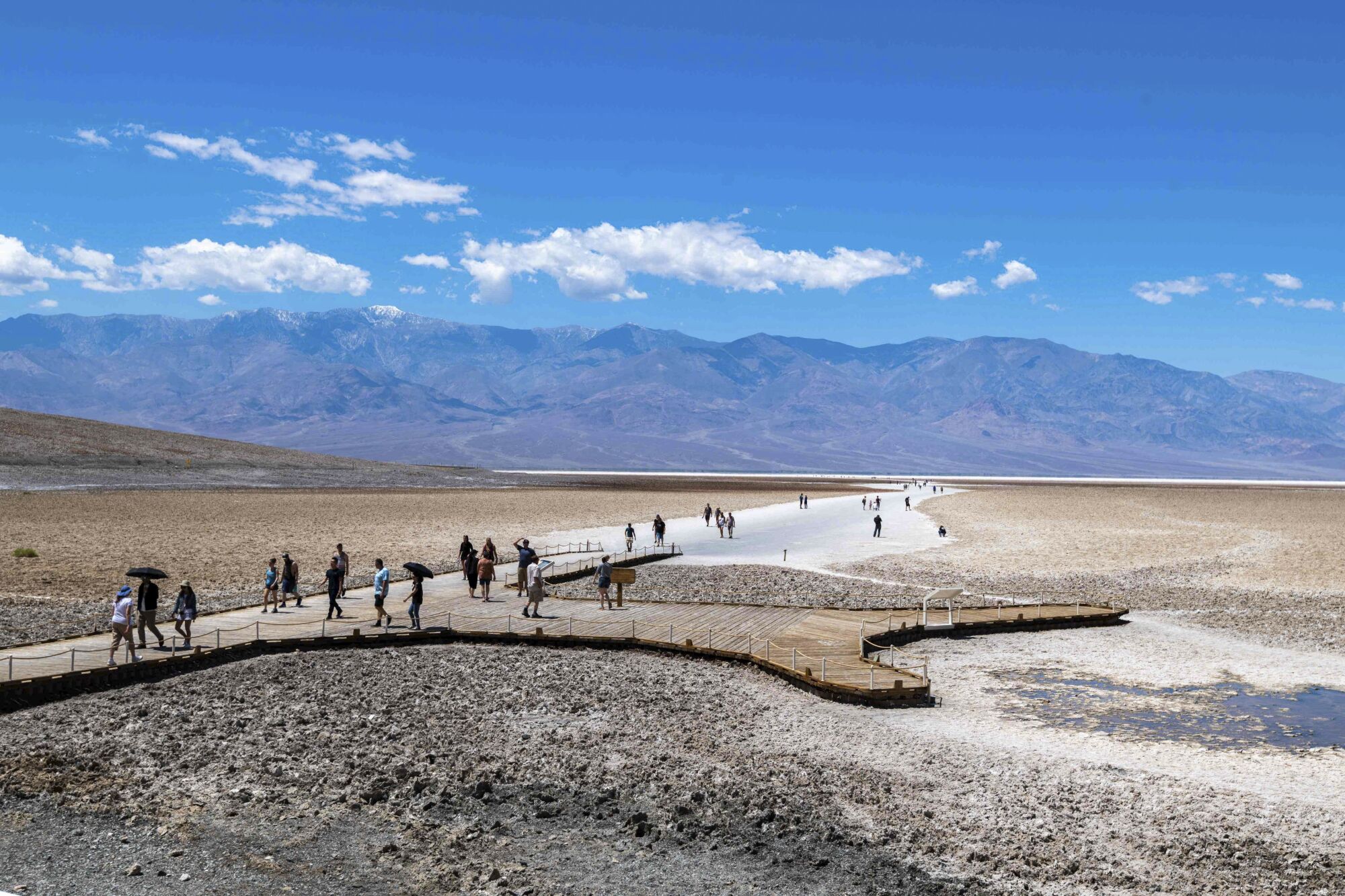 People walk in Badwater Basin, a dry lake bed, with mountains in the distance.