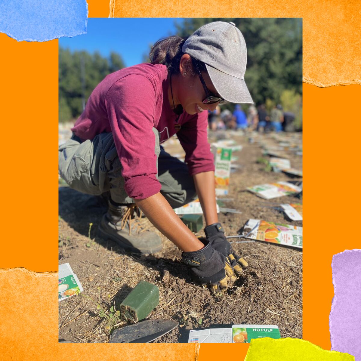 A woman in a billed cap and fingerless gloves kneels and digs her hands into dirt.