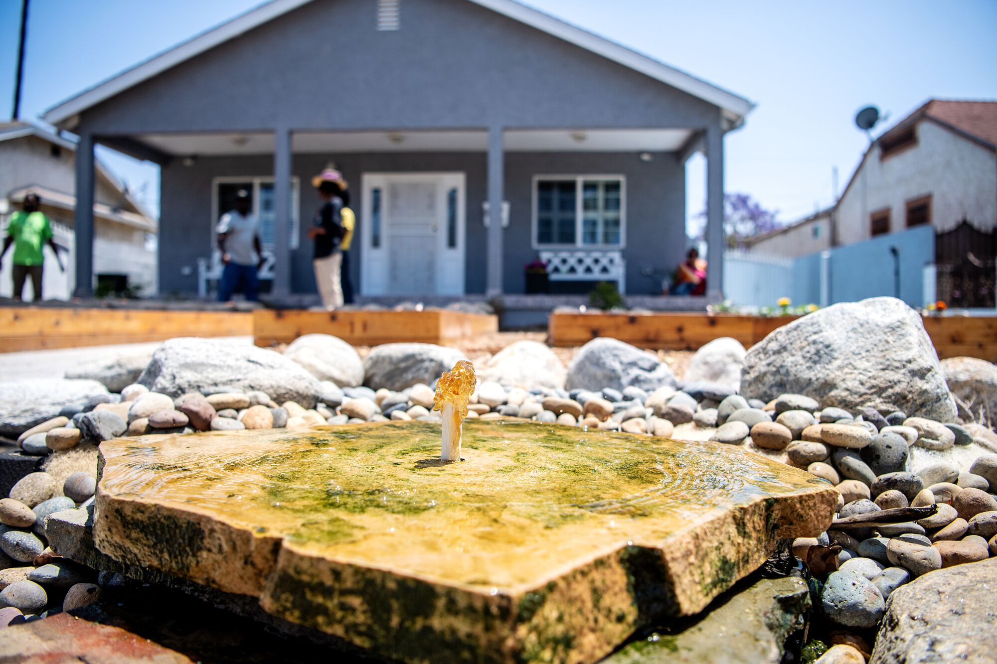 Water bubbles up from a pipe and flows out onto rocks in front of a house.