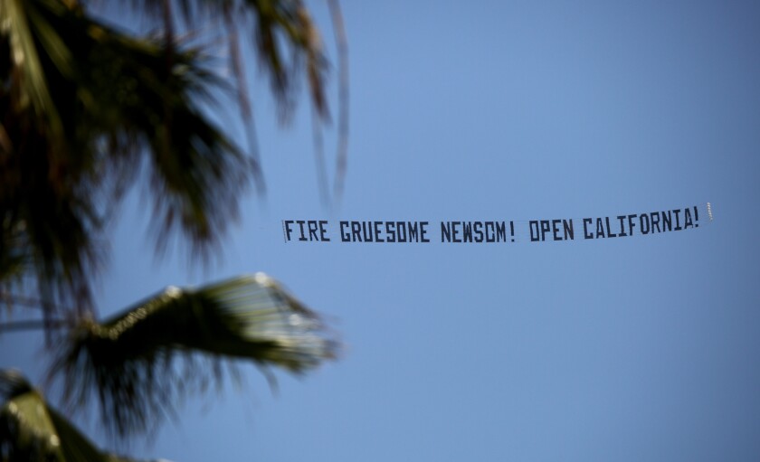 A small airplane flies a sign that reads "FIRE GRUESOME NEWSOM! OPEN CALIFORNIA!" during a protest over Huntington Beach on Friday.