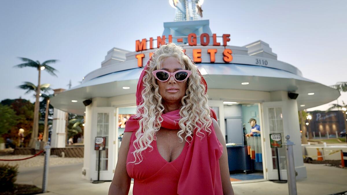 A woman dressed in pink stands in front of a mini-golf course.