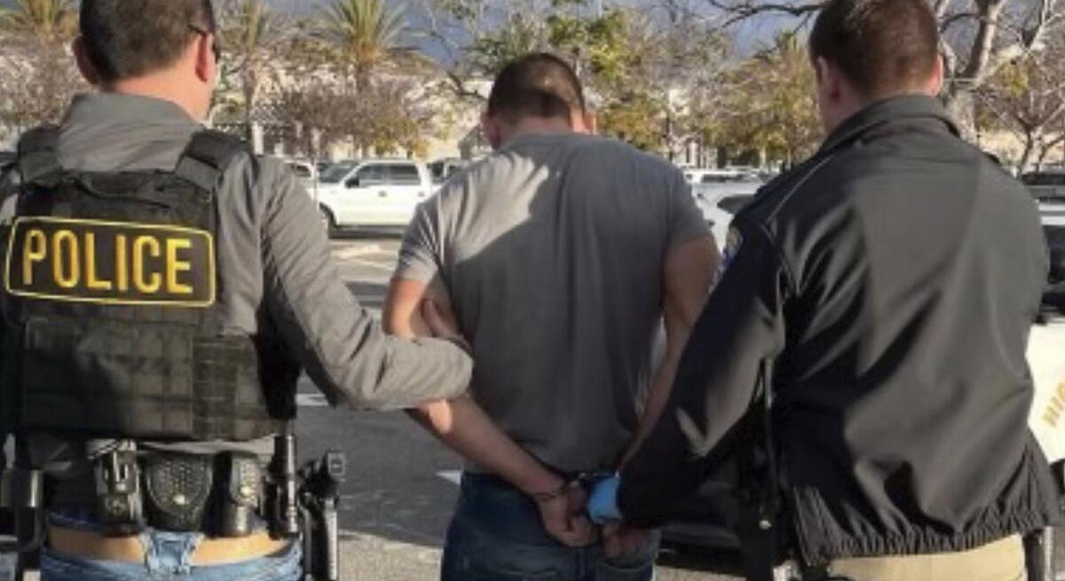 Police officers hold the arms of a man in handcuffs.