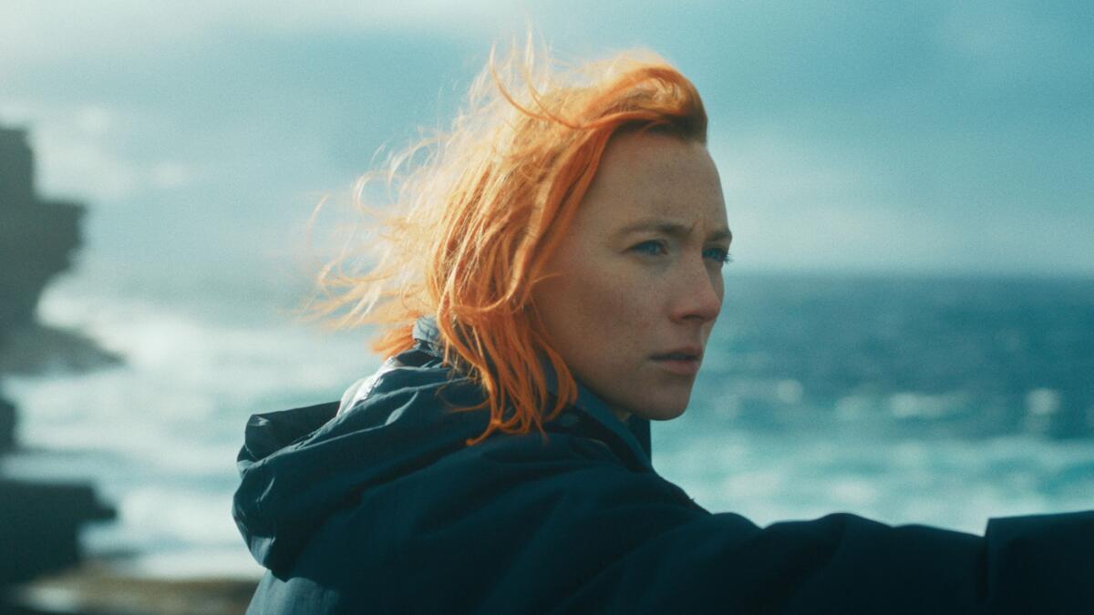 A woman with red hair looks over the sea.