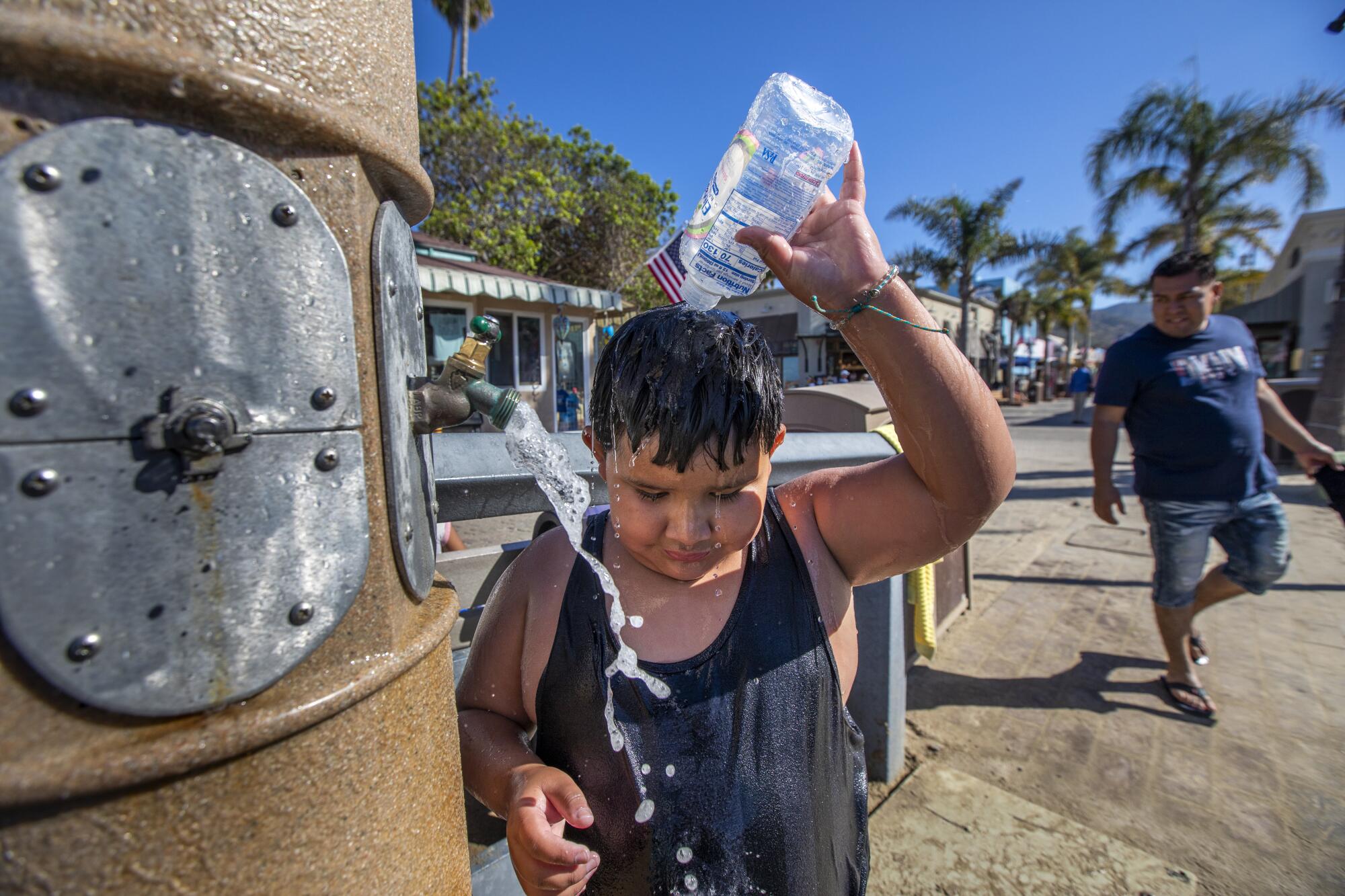 Raymond Valdez, 8, pours cool seawater on his head to rinse off the sand at the beach in Avalon.